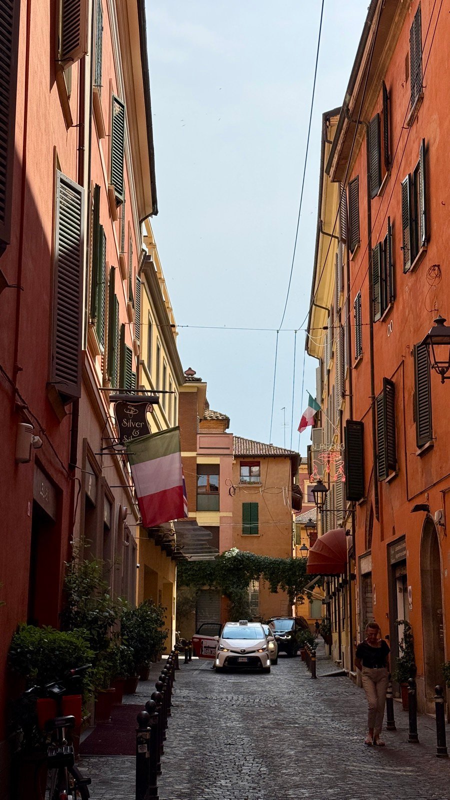 A quiet cobbled backstreet in central Bologna lined with ochre buildings and Italian flags