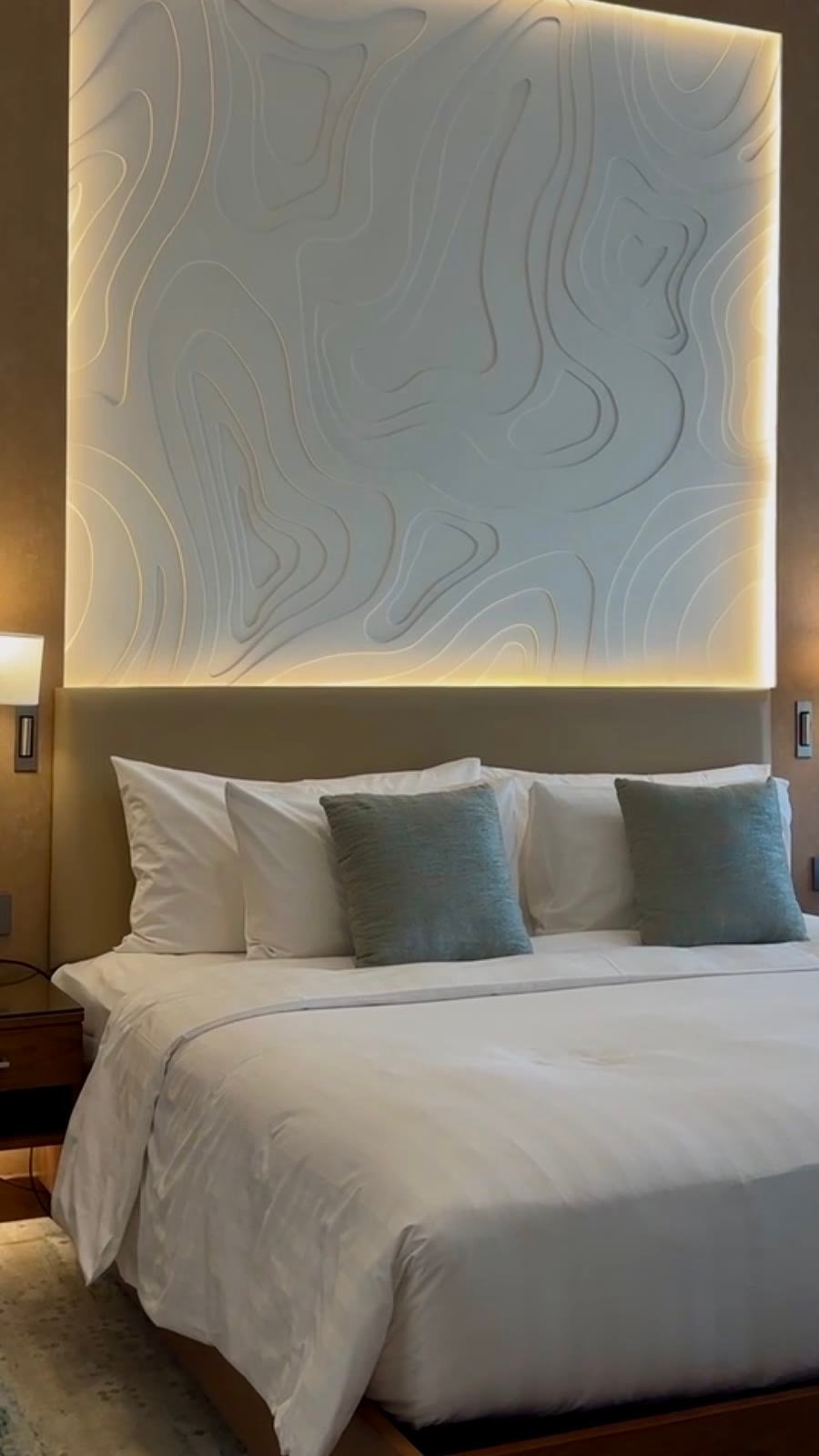 Modern bedroom with a backlit topographic headboard panel in the suite at dusitD2 Naseem Resort