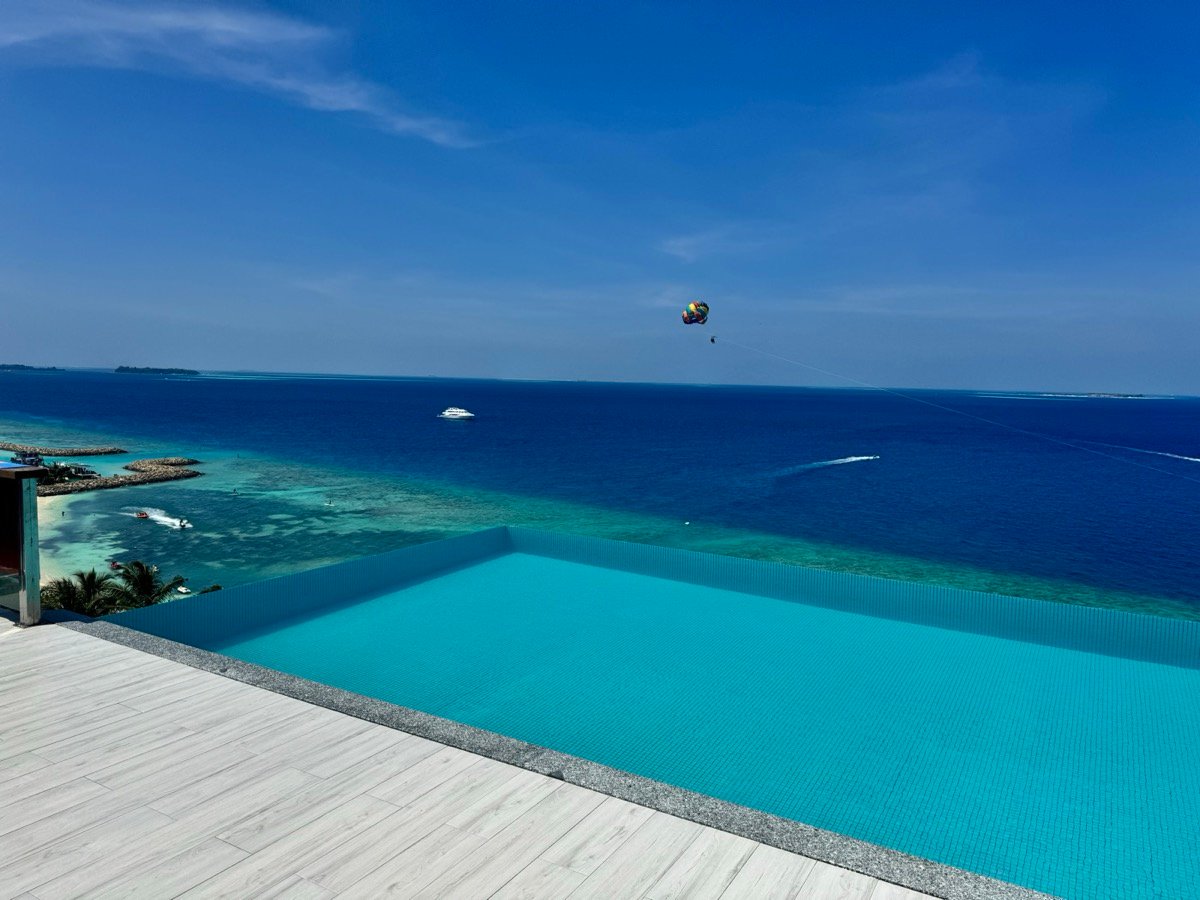 The rooftop infinity pool at Kaani overlooking the deep blue sea with a parasailer in the sky