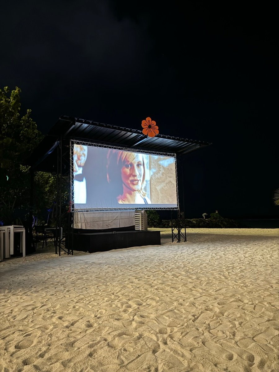 A free outdoor movie playing on a big screen on the sand at Kaani Beach Hotel at night