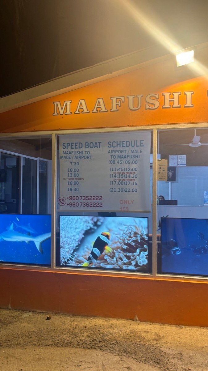 The speedboat schedule board outside a booking office on Maafushi at night