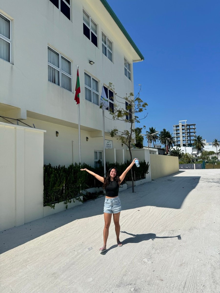 Alyssa with her arms up on a sunny sandy street on Maafushi