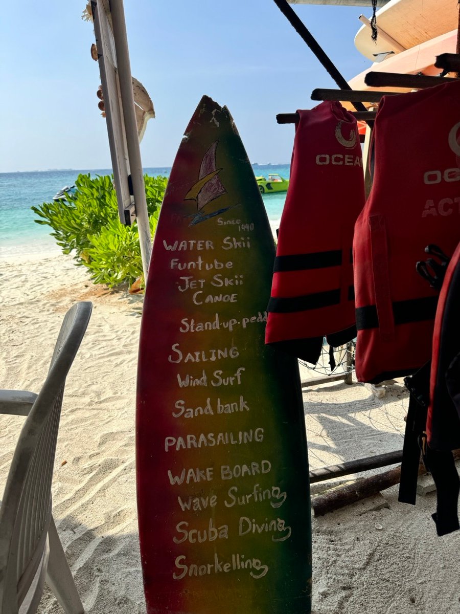 A painted surfboard listing water sports next to life jackets on the Maafushi beach