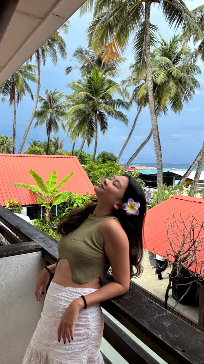 Alyssa on a balcony at Salt Beach Hotel with palm trees and red roofs behind her