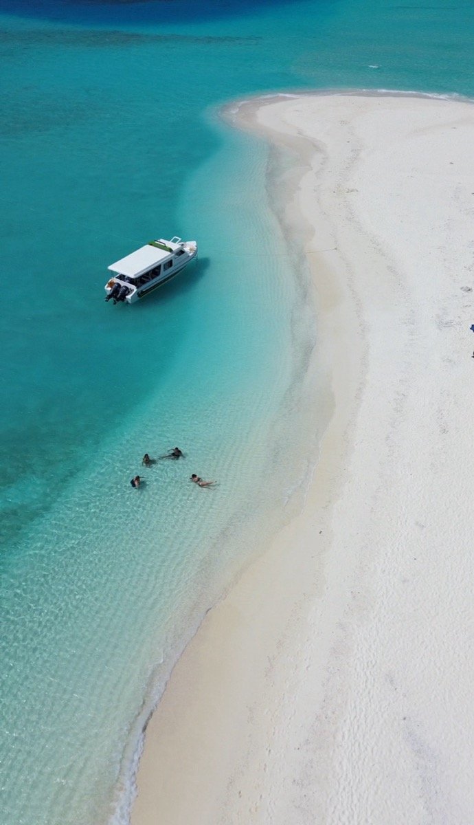 Drone shot of a white sandbank and a tour boat in turquoise water