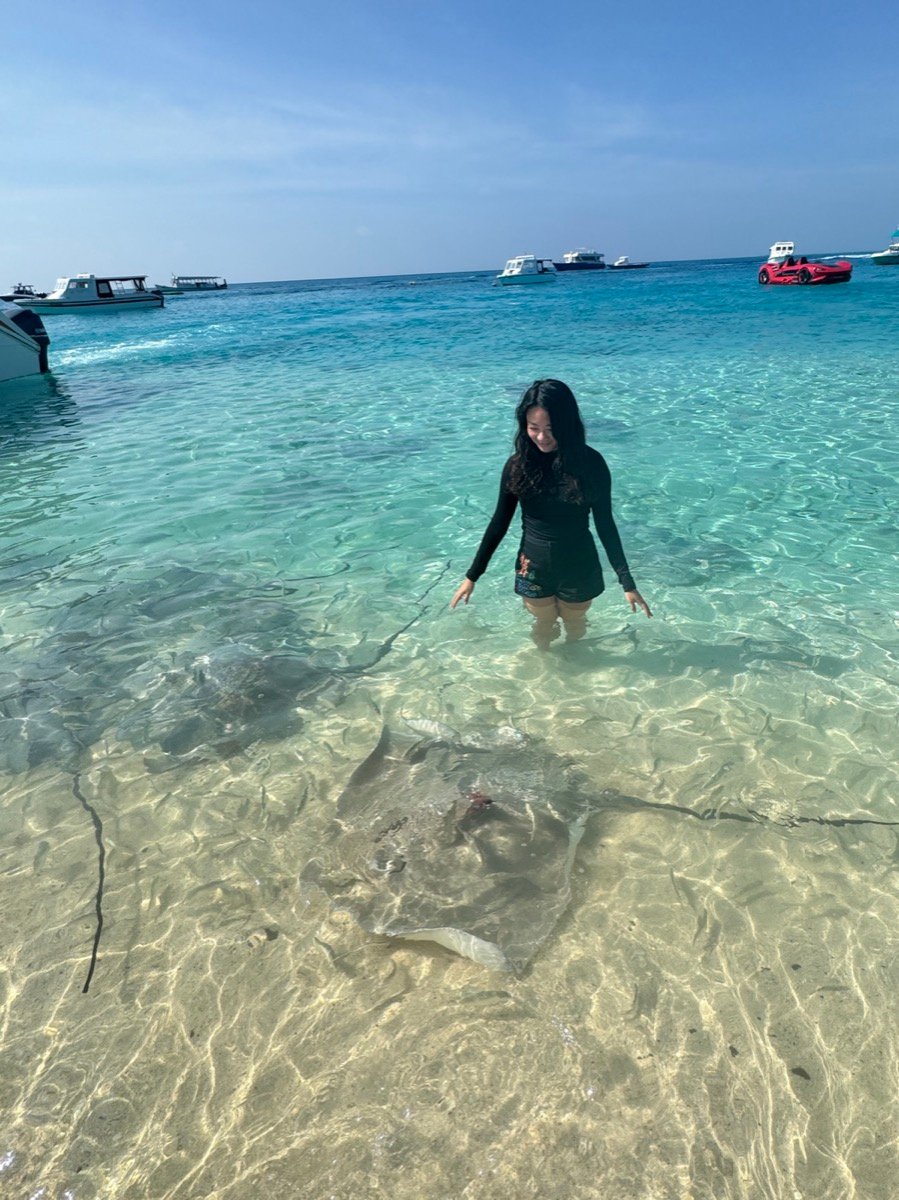 Alyssa standing in shallow turquoise water with stingrays swimming around her feet