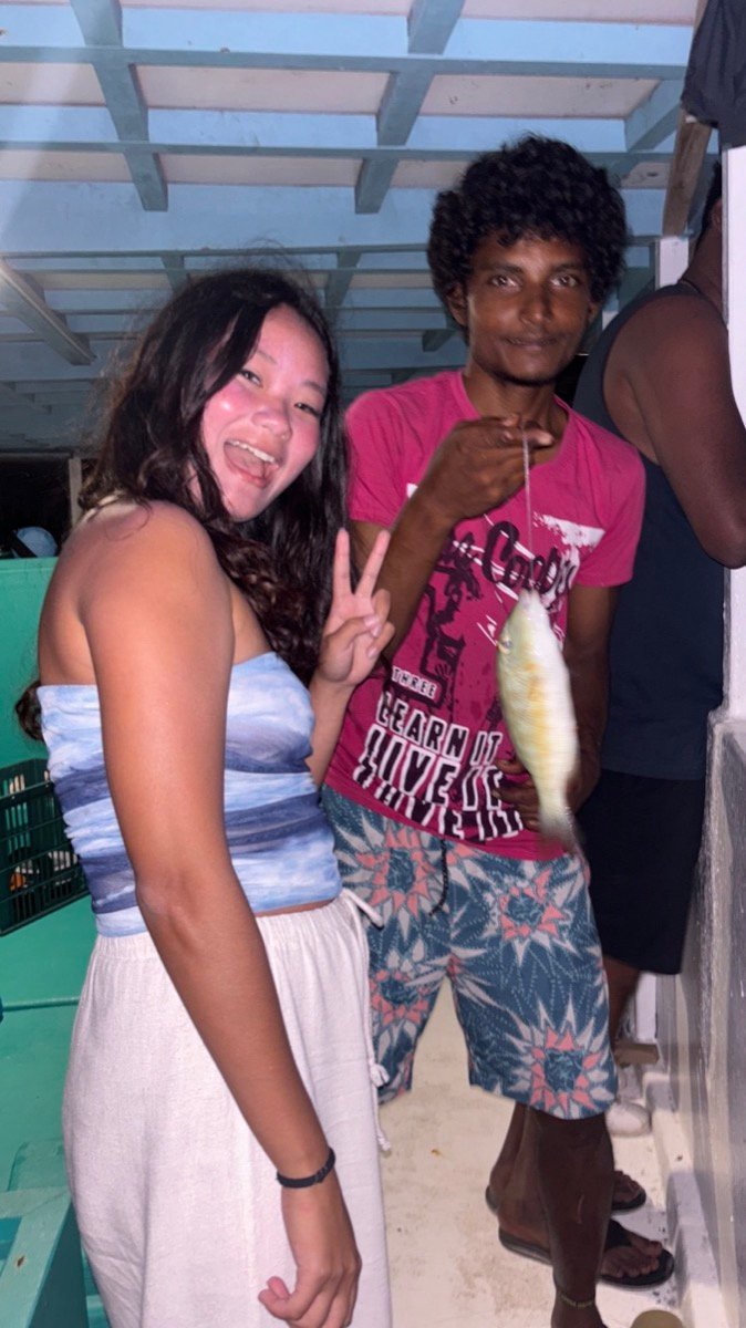 Alyssa with a local crew member holding up a small fish on the fishing boat