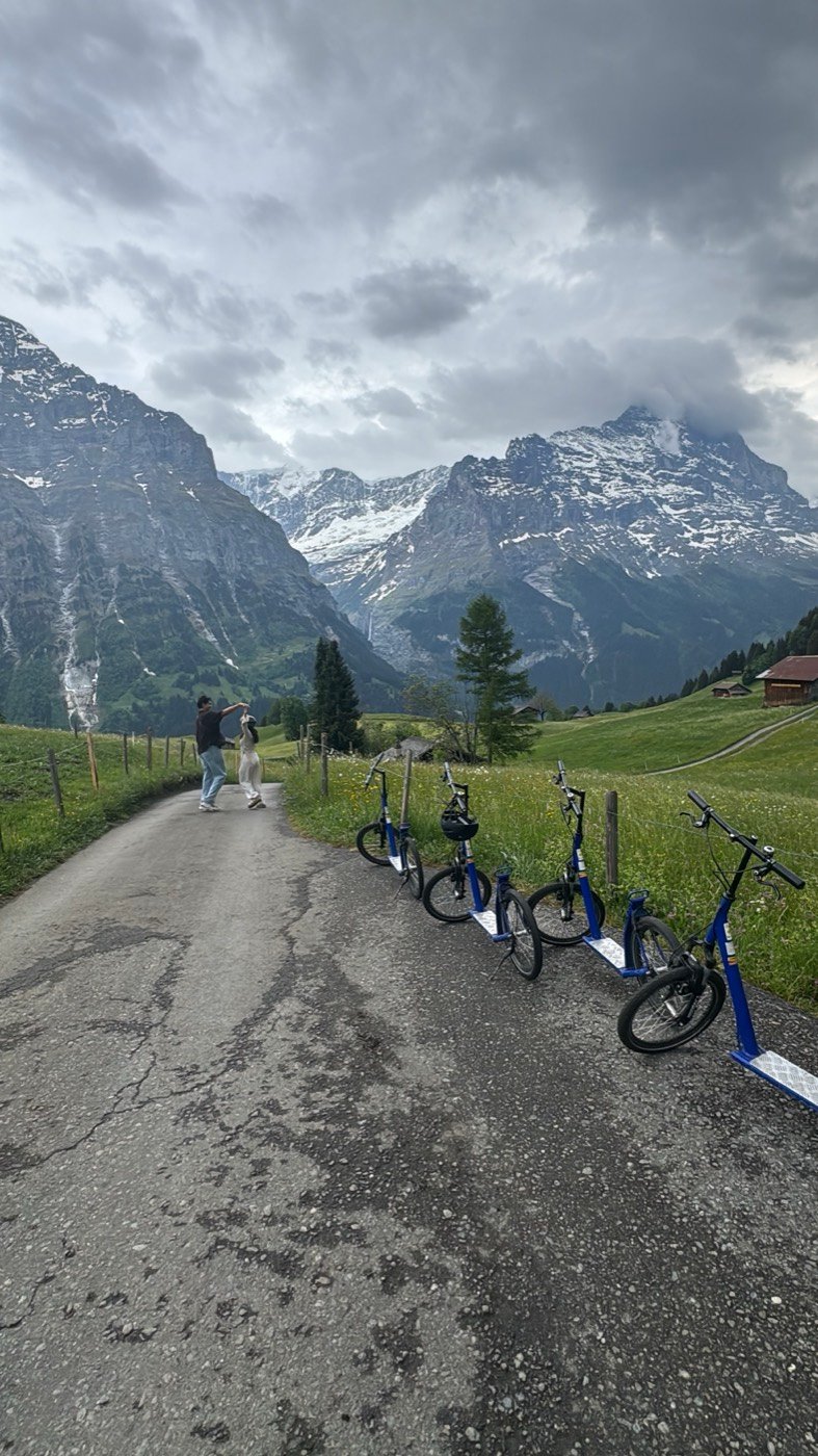 A row of blue Trottibike scooter-bikes parked along a mountain path below the Eiger, ready for the ride down