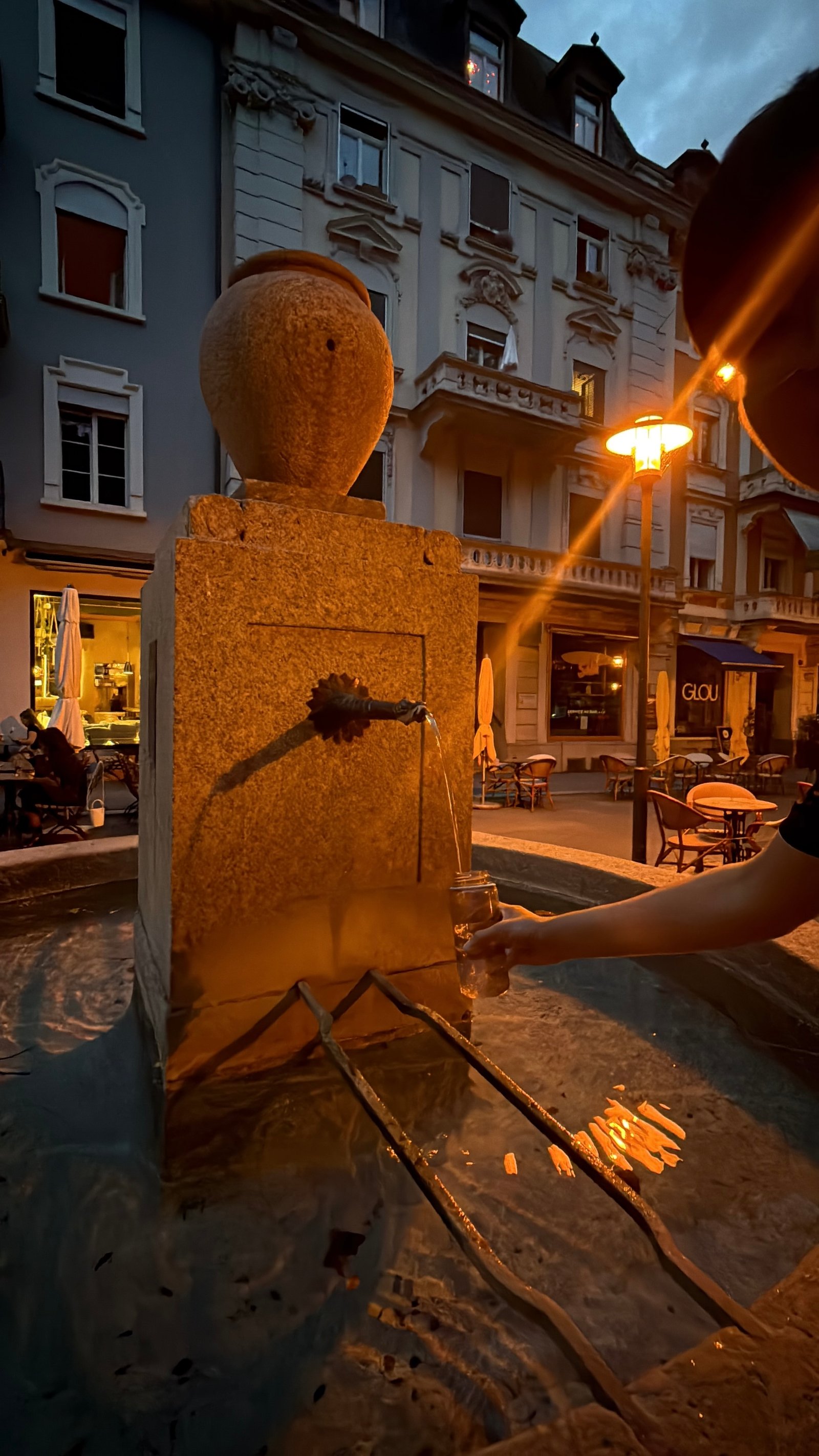 Filling a glass from a stone public drinking fountain in Luzern's old town at dusk