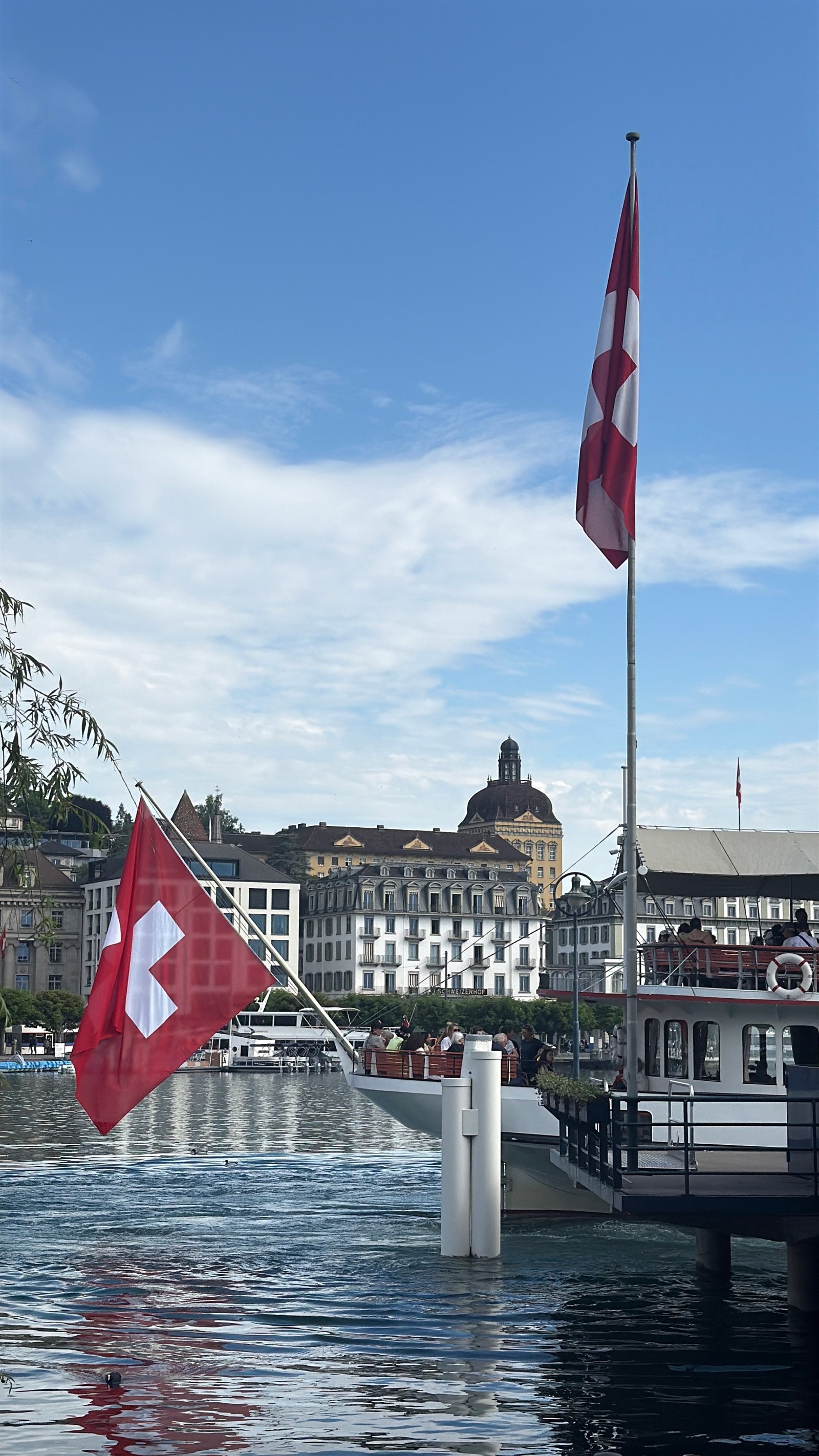 Swiss flag flying beside a lake boat on Lake Luzern, with the old-town lakefront behind